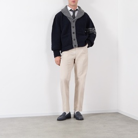 Model wearing Thom Browne navy wool cardigan with grey contrast trim and 4-bar stripe detail, styled with cream trousers and a tie.