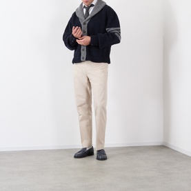 Model wearing Thom Browne navy wool cardigan with grey varsity stripe trim, styled with beige trousers and black loafers.
