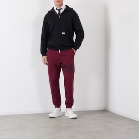 Model wearing Thom Browne burgundy cotton sweatpants with 4-bar stripe detail, styled with black zip hoodie and white trainers