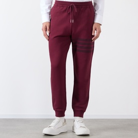 Model wearing Thom Browne burgundy cotton sweatpants with four-bar stripe detail, styled with white trainers.