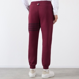 Model wearing Thom Browne burgundy cotton sweatpants with signature 4-bar stripe detail, styled with white trainers.