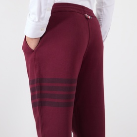 Model wearing Thom Browne burgundy cotton sweatpants with tonal four-stripe detail at leg, styled with white shirt.