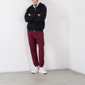 Model wearing Thom Browne burgundy cotton sweatpants with 4-bar stripe detail, styled with black zip hoodie and white trainers