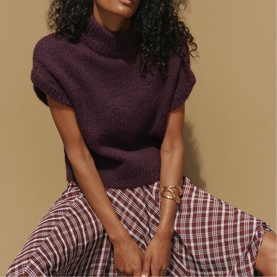 Model wearing Mint Velvet red turtleneck short-sleeve knit top, styled with red plaid midi skirt and gold cuff bracelet.
