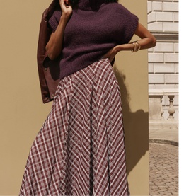 Model wearing Mint Velvet red plaid maxi skirt, styled with a dark plum knit top and gold bracelets