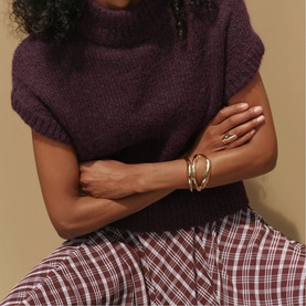 Model wearing Mint Velvet red check wide-leg trousers, styled with a purple knit short-sleeve top and gold bangles.