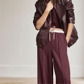 Model wearing Mint Velvet red wide-leg trousers with drawstring waist, styled with a burgundy leather jacket and matching top.