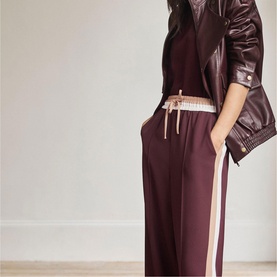 Model wearing Mint Velvet red wide-leg trousers with side stripe, styled with a burgundy leather jacket and cropped top.