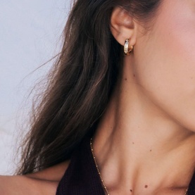 Model with Mettle & Bloom gold hoop earrings featuring crystal-set detailing, styled with a burgundy top