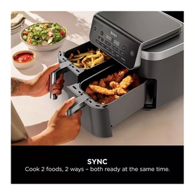 Ninja dual-zone air fryer with both baskets open, showing fries and chicken wings cooking simultaneously, grey and black finish