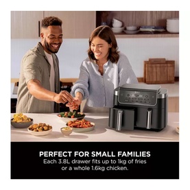 Couple cooking with a large black dual-drawer air fryer on a kitchen counter, surrounded by prepared food dishes