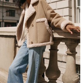 Model wearing Mint Velvet brown shearling jacket with cream fleece trim, styled with light blue wide-leg jeans