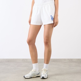 Model wearing Sporty and Rich white cotton shorts with blue LA Dodgers graphic, styled with white ankle socks and grey trainers.