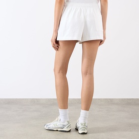 Model wearing Sporty and Rich white cotton shorts, styled with white ankle socks and grey chunky trainers