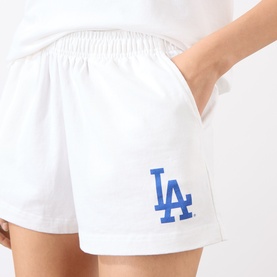 Model wearing Sporty and Rich white cotton shorts with blue LA Dodgers logo embroidery, elasticated waist, styled with white top.