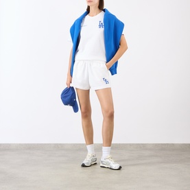 Model wearing Sporty and Rich White Team Blue cotton shorts with LA Dodgers logo, styled with matching tee, blue vest and cap, white trainers.