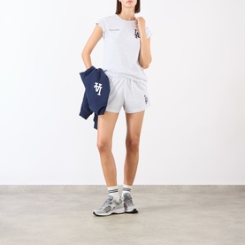 Model wearing Sporty & Rich Heather Gray Navy shorts with matching white tee, carrying navy jacket, styled with white socks and grey trainers.