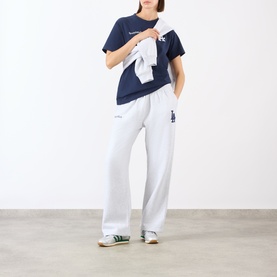 Model wearing Sporty and Rich Heather Gray Navy Sweat Bottom with navy graphic tee, carrying white zip-up, styled with green trainers.