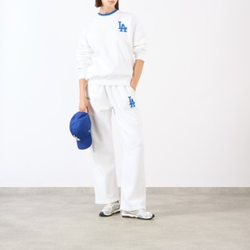 Model wearing Sporty and Rich White Team Blue LA sweat top and matching wide-leg joggers, styled with a blue cap and white trainers.