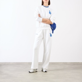 Model wearing Sporty and Rich White Team Blue cotton sweat top with matching wide-leg joggers, styled with a blue cap and white trainers.