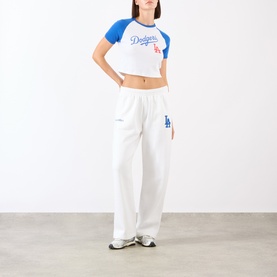 Model wearing Sporty and Rich White Team Blue cotton sweat bottoms with wide leg, styled with matching LA Dodgers crop tee and white trainers.