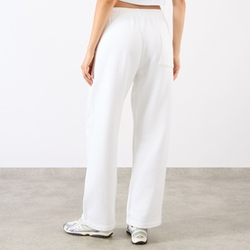 Model wearing Sporty and Rich White Team Blue Sweat Bottoms, rear view, wide-leg silhouette with elasticated waistband, styled with white trainers.