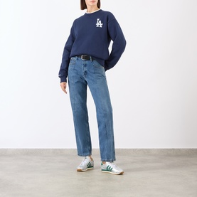Model wearing Sporty and Rich Dark Navy White cotton sweat top with LA logo, styled with mid-wash straight jeans and green trainers.