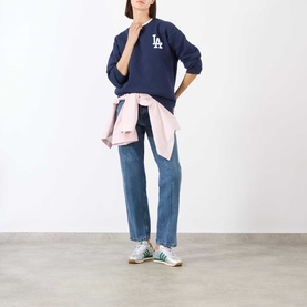 Model wearing Sporty and Rich Dark Navy White cotton sweat top with blue jeans, pink shirt tied at waist, and green trainers.