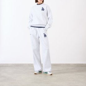 Model wearing Sporty and Rich Heather Gray Navy sweatshirt and matching wide-leg sweatpants with LA logo, styled with green trainers.