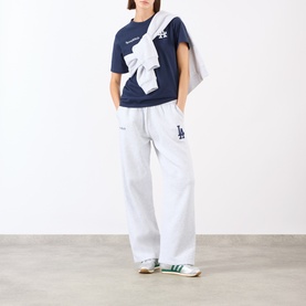 Model wearing Sporty and Rich dark navy cotton T-shirt with white graphic, styled with white wide-leg joggers and green trainers.