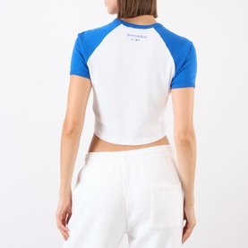 Model wearing Sporty and Rich crop top in white with team blue raglan sleeves, rear view, styled with white wide-leg trousers