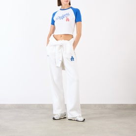 Model wearing Sporty and Rich white and blue raglan crop top with LA Dodgers logo, styled with white wide-leg joggers and white trainers