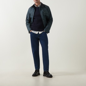 Model wearing Belstaff Dark Ink crew neck knit, styled with green jacket, white shirt, blue jeans and black boots.