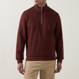Model wearing Belstaff Half Zip sweatshirt in oxblood, small logo chest badge, styled with beige chinos