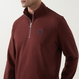 Model wearing Belstaff oxblood cotton half-zip sweatshirt with silver zip and embroidered logo badge at chest