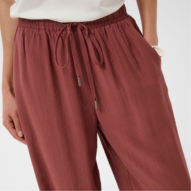 Model wearing Kaffe henna wide-leg drawstring trousers with elasticated waistband, styled with a white top and gold bracelet.