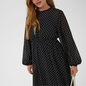 Model wearing Kaffe black and white dot midi dress with balloon sleeves and belted waist, carrying a white bag