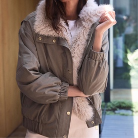 Model wearing Mint Velvet green oversized jacket with faux fur collar and gold-tone snap buttons, styled with blush trousers