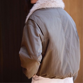 Model wearing Mint Velvet green bomber jacket, back view, with fluffy white faux fur collar detail.