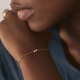 Model with Missoma gold chain bracelet featuring a single round clear stone, worn on wrist, styled with blue top and gold ring