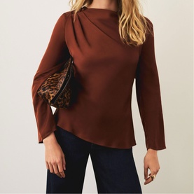 Model wearing rust brown draped neck long-sleeve top with flared cuffs, styled with dark jeans and leopard print bag