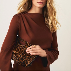 Model carrying a leopard-print calf-hair mini shoulder bag with gold-tone hardware, styled with a rust long-sleeve dress