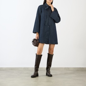 Model wearing FRAME DENIM Rinse denim dress with tie neck, styled with dark brown knee-high boots and small brown bag.