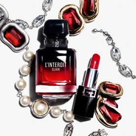 Givenchy L'Interdit Elixir Eau De Parfum bottle styled with red lipstick, pearl necklace, crystal and ruby jewellery on white background.