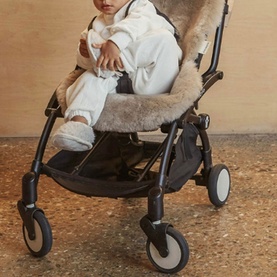 BiniBamba Toast sheepskin stroller liner in warm beige, shown on black pushchair with infant seated, wearing cream outfit