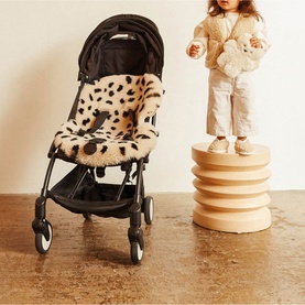 BiniBamba Leopard pram liner in cream and brown spot print, fitted to a black stroller, with a toddler standing on a wooden stool nearby