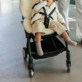 BiniBamba Milk sheepskin pram liner shown in use on a black stroller, with a baby seated wearing a cream outfit
