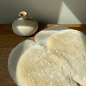 BiniBamba Milk sheepskin rug, cream fluffy round shape, styled on wooden surface beside a ceramic vase