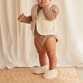 Model wearing BiniBamba Milk fleece baby booties, styled with a cream sherpa vest and brown ribbed bodysuit