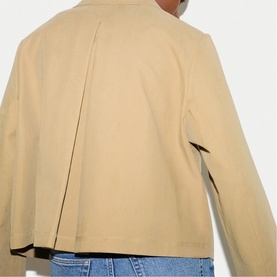 Model wearing Jigsaw beige jacket, back view showing centre pleat detail, styled with blue jeans.